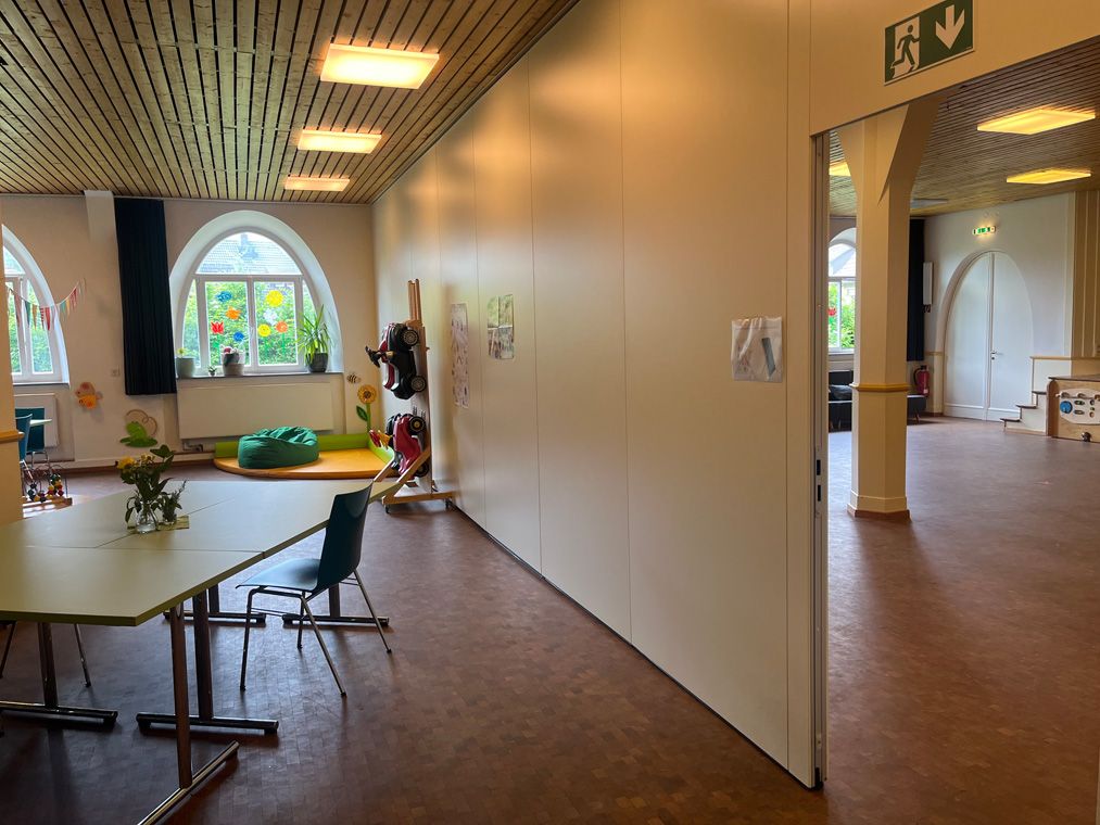 Getrennter Raum mit Tischen und Stühlen, Blick durch eine Trennwand in den Saal.