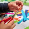 Kinderhände schneiden bunte Papierstreifen mit Schere