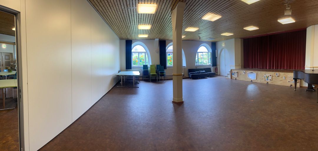 Großer Saal mit Bühne, roten Vorhängen und leeren Flächen.